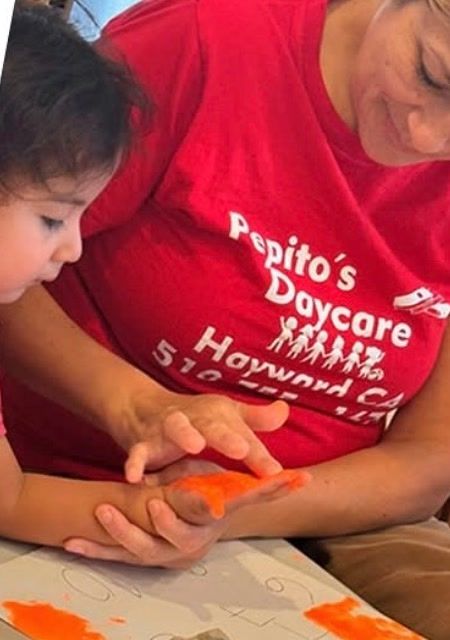A caregiver helping a toddler make orange handprints