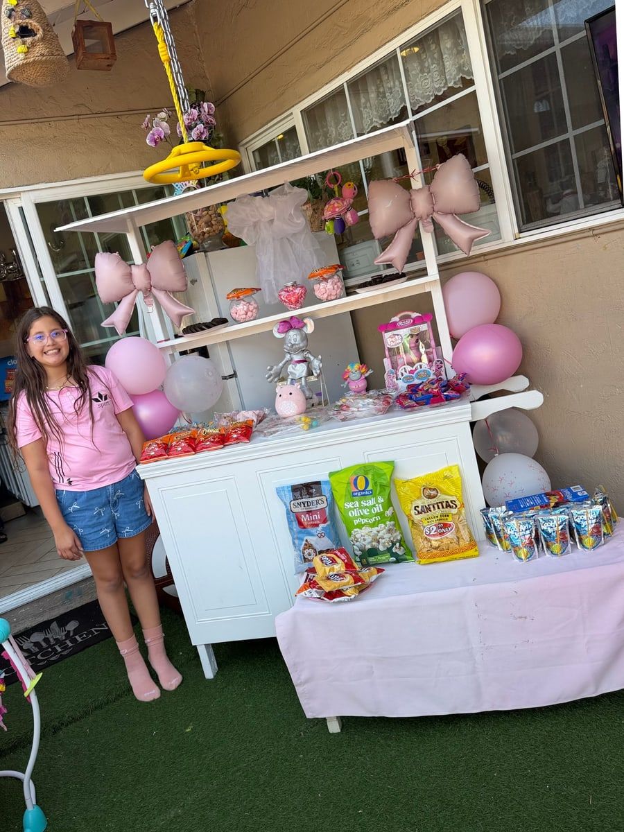 A girl next to a candy cart decorated with pink balloons and bows