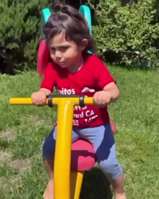 A toddler riding a yellow rocking toy on the grass