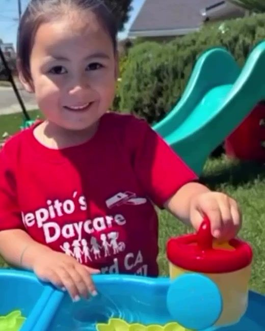 A smiling toddler playing at a blue water table